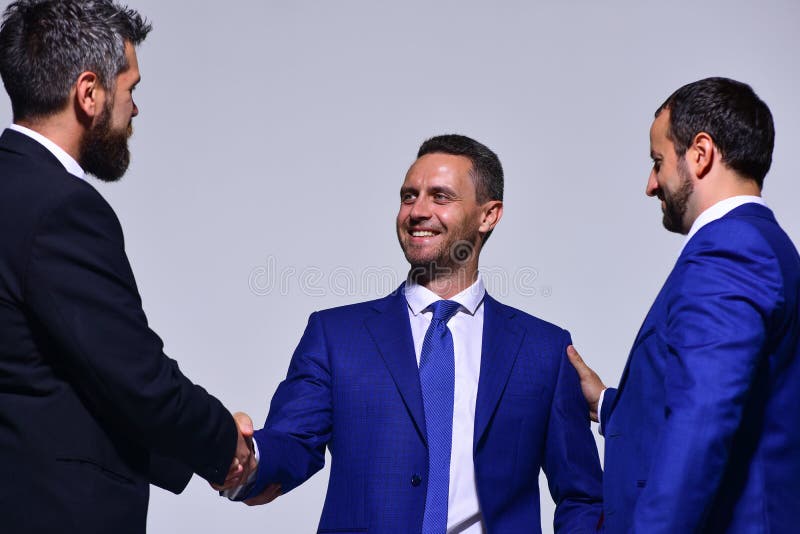 Businessmen with happy faces in formal wear on grey background. Business relationship and support concept. Coworkers or partners shake hands for cooperation. Leaders have business meeting making deal