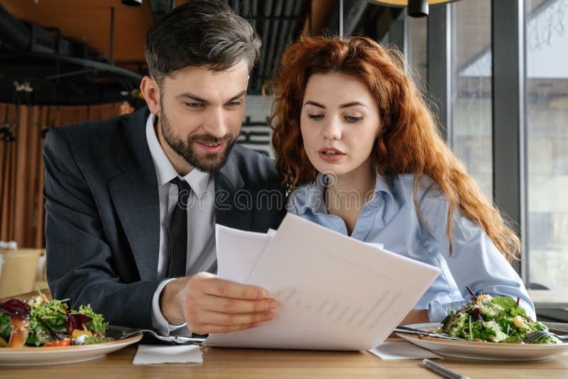 Businesspeople having business lunch at restaurant sitting eating reading documents stock photo Businesspeople having business lunch at restaurant sitting eating reading documents stock photo