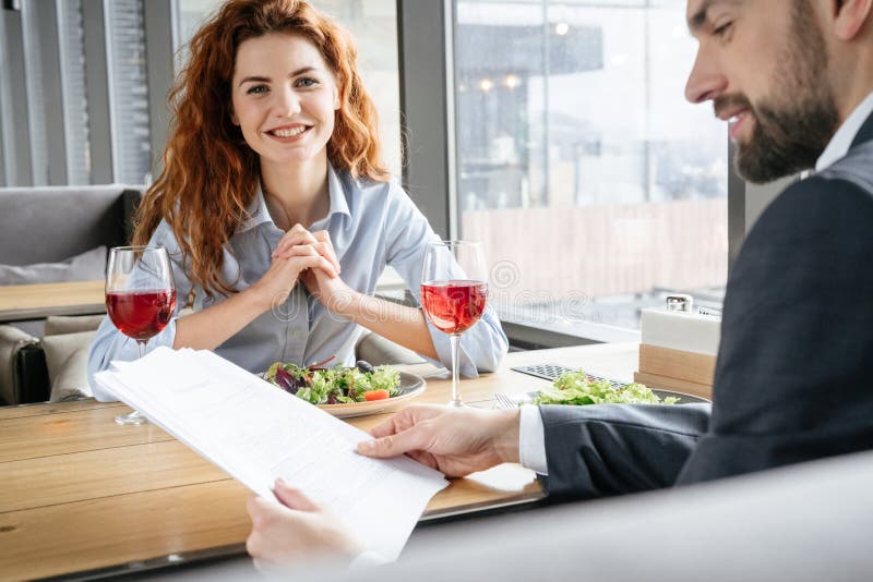 Businesspeople som har affärslunch på restaurangen som sitter äta sallad som dricker vinmannen som läser dokument medan kvinna royaltyfri foto Businesspeople som har affärslunch på restaurangen som sitter äta sallad som dricker vinmannen som läser dokument medan kvinna royaltyfri foto