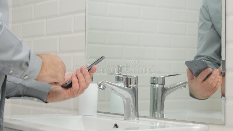 Businessperson in Badkamers die Zijn Mobiele Telefoontekst gebruiken vóór het Wassen van Handen stock foto Businessperson in Badkamers die Zijn Mobiele Telefoontekst gebruiken vóór het Wassen van Handen stock foto