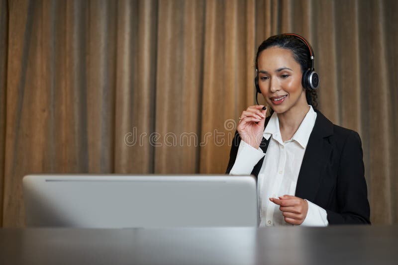 Businessperson Engaged in a Virtual Meeting Using a Computer and Headset in a Professional Setting. A professional businessperson wearing formal attire and a headset, engaged in an online meeting via a computer. The setting portrays focus and connectivity, suggesting a business or customer service environment.