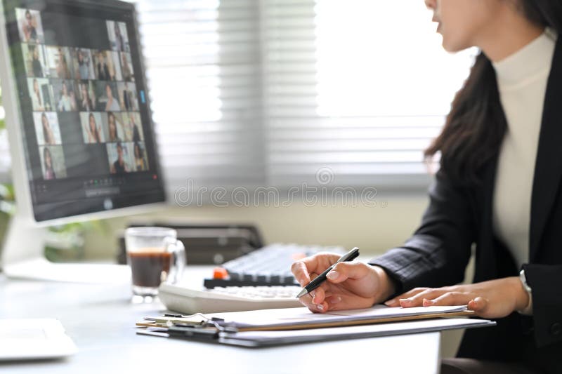 Businesswoman attending a virtual meeting, taking notes while focused on computer screen stock image