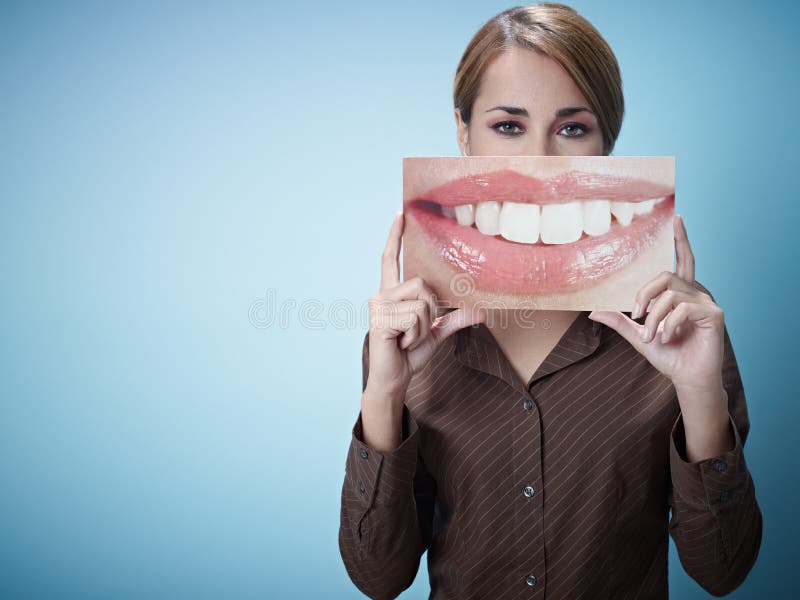 Mid adult business woman holding photo of toothy smile on blue background. Horizontal shape, front view, waist up, copy space. Mid adult business woman holding photo of toothy smile on blue background. Horizontal shape, front view, waist up, copy space