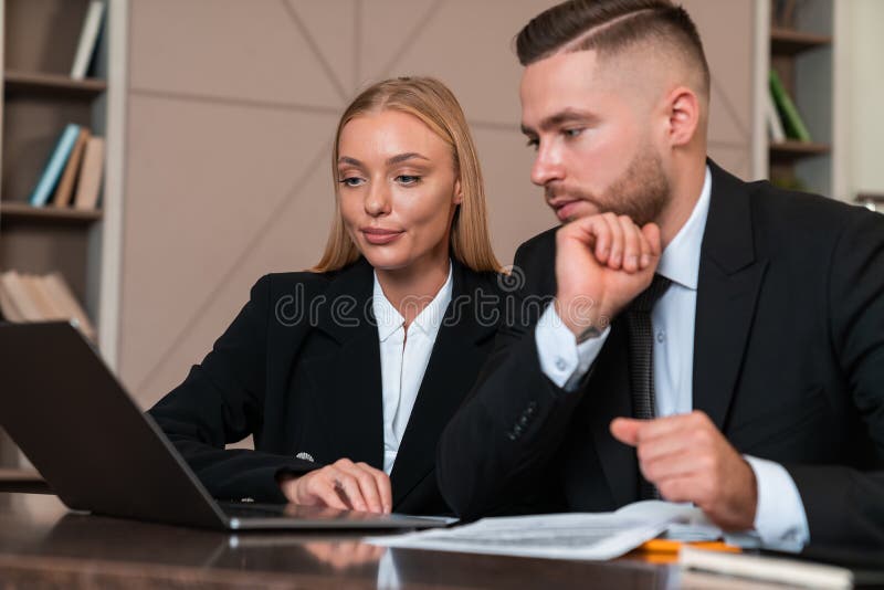 Businesswoman and businessman wearing formal wear sitting working on laptop stock photo