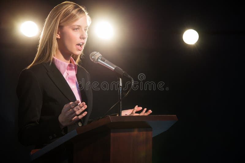 Businesswoman Giving Speech At Podium In Auditorium