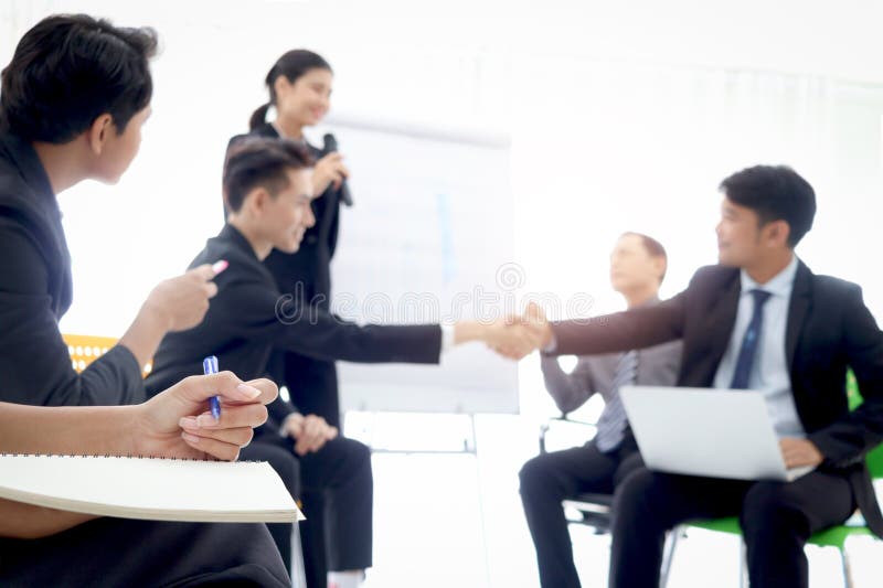 Businesswoman hand holding a pen ready for taking note at the meeting with blurred background of businesspeople group at