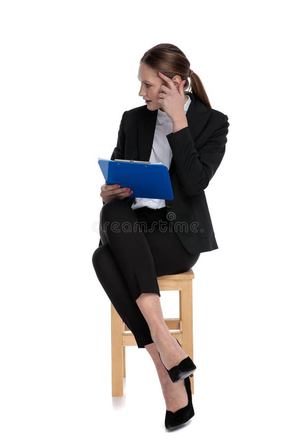 Sexy businesswoman wearing black suit sitting and holding clipboard while making a mad sign to her head against white background. Sexy businesswoman wearing black suit sitting and holding clipboard while making a mad sign to her head against white background