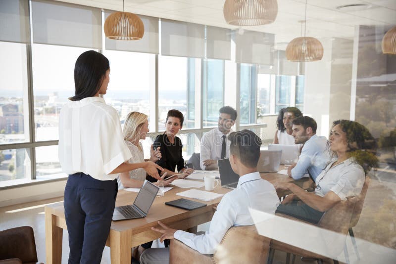 Businesswoman Leads Meeting Around Table Shot Through Door