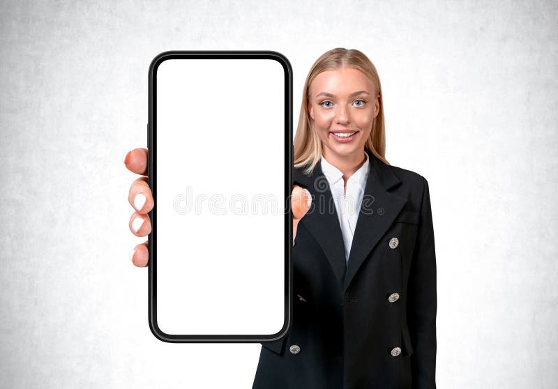Businesswoman with mockup display smartphone on grey background. Smiling businesswoman showing phone with large mock up copy space screen, grey background. Concept of mobile app and social media