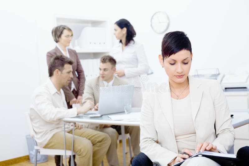 Businesswoman sitting in front, holding personal organizer,reading. Four businesspeople working with laptop computer in background. Laptop personal computer stock images, royalty-free photos and pictures