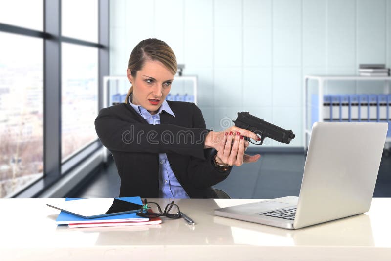 Businesswoman pointing gun to computer laptop sitting at desk desperate and stressed