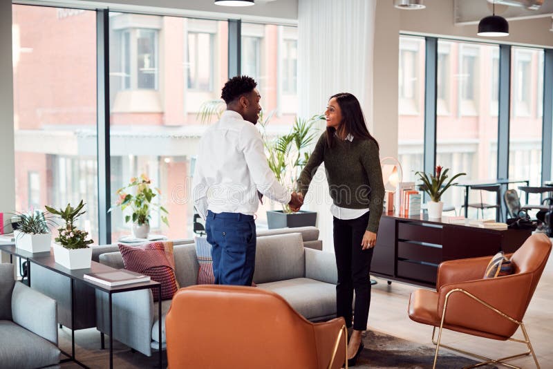 Businesswoman Shaking Hands With Male Interview Candidate In Seating Area Of Modern Office