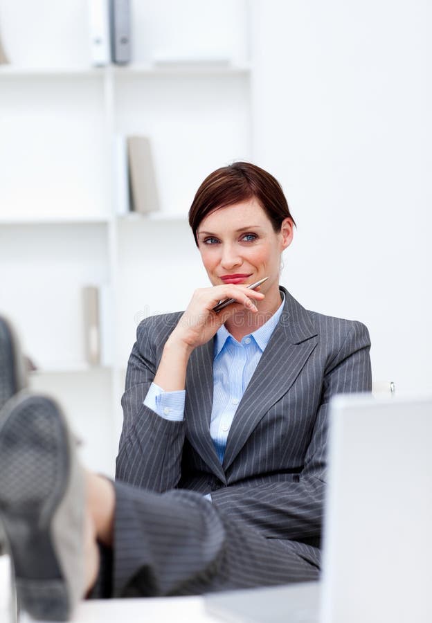 Satisfied Businesswoman sitting in office with feet on desk against white background