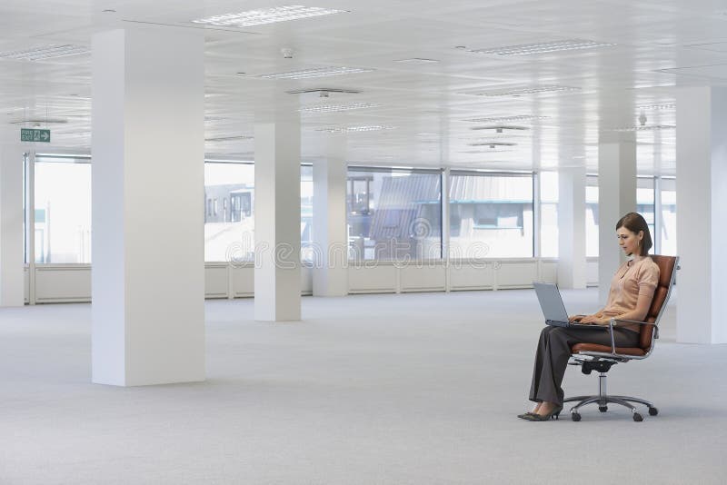 Businesswoman Using Laptop On Chair In Empty Office stock image