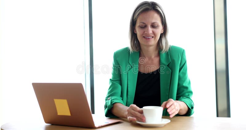 Businesswoman works on laptop and drinks tea coffee or water with cup