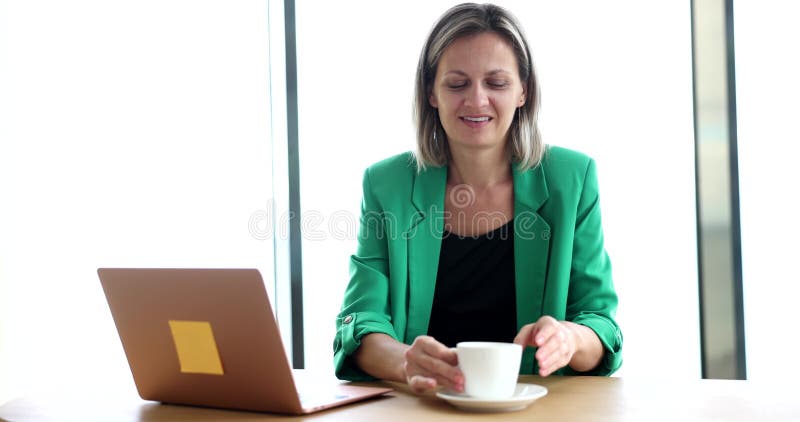 Businesswoman works on laptop and drinks tea coffee or water with cup