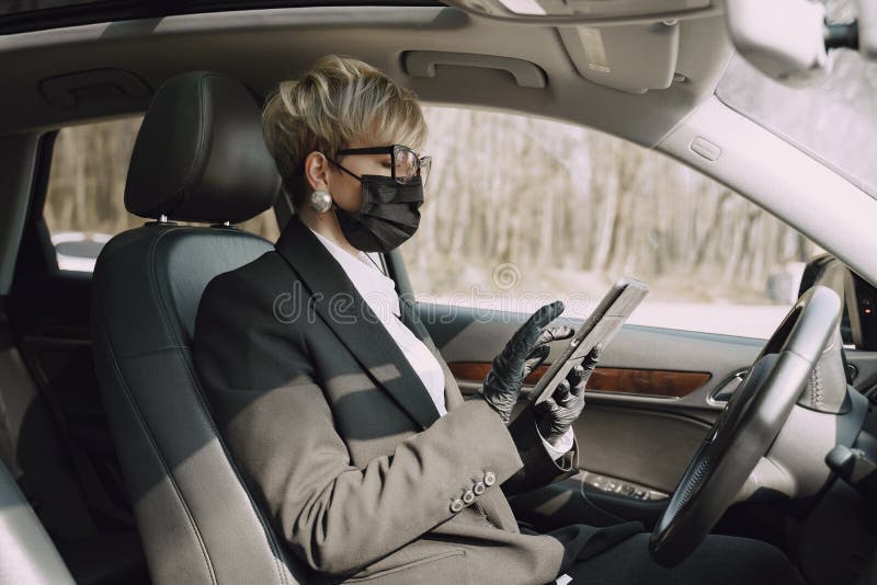 Businesswoman in a black mask sitting inside a car