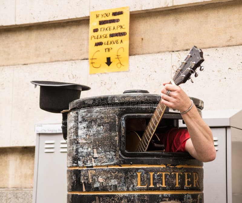 Busker singing and playing guitar inside a rubbish bin