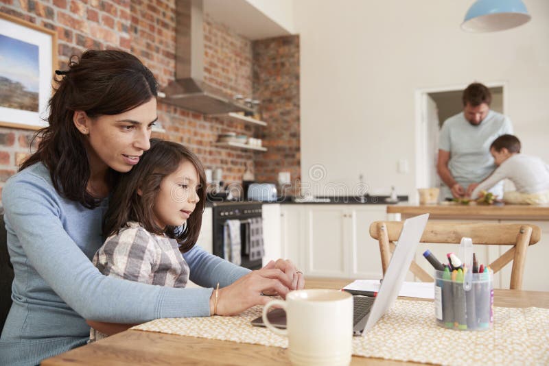 Busy Family Home With Mother Working As Father Prepares Meal