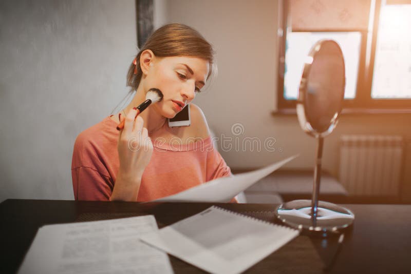 Busy woman making a make-up, talking on the phone, reading documents at the same time. Businesswoman doing multiple tasks. Multitasking business person. Busy woman making a make-up, talking on the phone, reading documents at the same time. Businesswoman doing multiple tasks. Multitasking business person.