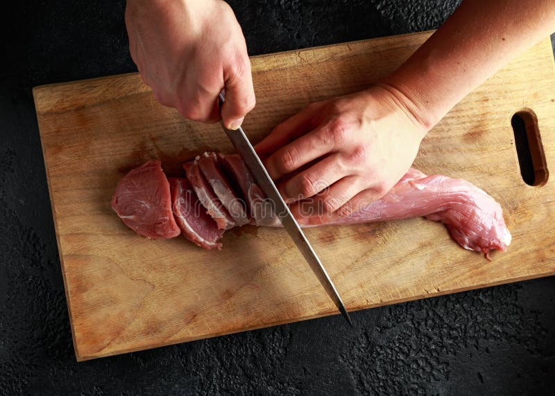 Butcher`s hands ready to cut with a knife raw pork tenderloin fillet on wooden board. stock photos Butcher`s hands ready to cut with a knife raw pork tenderloin fillet on wooden board. stock photos