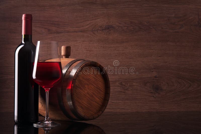 Bottle of red wine, glass and barrel on dark wooden background. Bottle of red wine, glass and barrel on dark wooden background