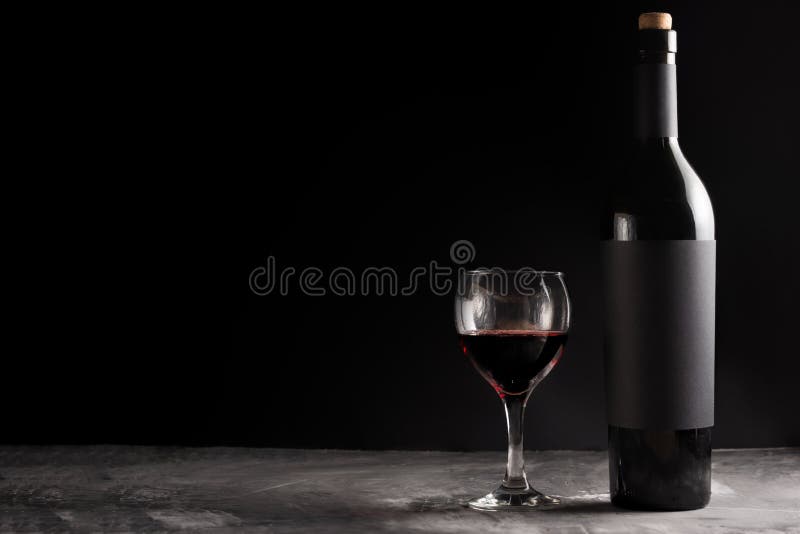 A bottle of red expensive wine with a black blank label on a dark background with a glass of red wine. Wine bottle mockup with space for text. A bottle of red expensive wine with a black blank label on a dark background with a glass of red wine. Wine bottle mockup with space for text.