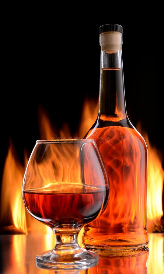 Bottle and glass of cognac over dark background with flame. Bottle and glass of cognac over dark background with flame