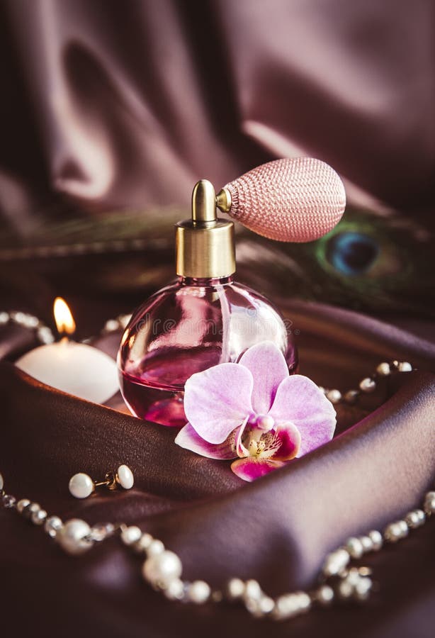 Butelka perfum i perłowa biżuteria z natomizatora na jedwabistym ciemnym różowym tkaninie z piórkiem peacock i płonącą świecą. obraz royalty free