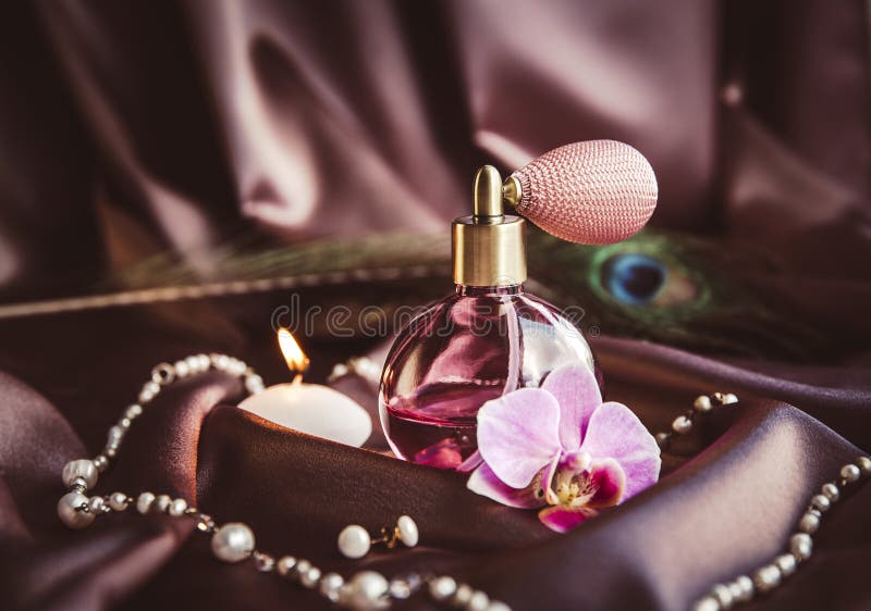 Butelka perfum i perłowa biżuteria z natomizatora na jedwabistym ciemnym różowym tkaninie z piórkiem peacock i płonącą świecą. obrazy royalty free