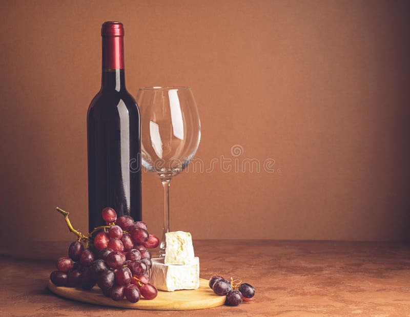 A bottle of wine an empty glass of a bunch of red grapes a slice of cheese on a dark background. Copy space. Selective focus. Horizontal frame. A bottle of wine an empty glass of a bunch of red grapes a slice of cheese on a dark background. Copy space. Selective focus. Horizontal frame
