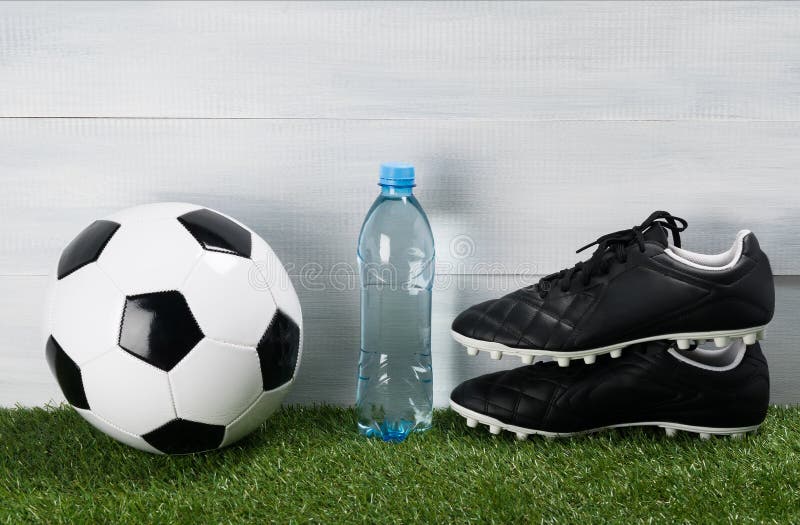 Butelka woda na zielonym gazonie obok butów dla futbolu i piłki obrazy stock Butelka woda na zielonym gazonie obok butów dla futbolu i piłki obrazy stock