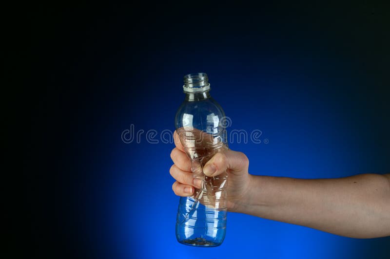 Horizontal image of a hand crushing a recyclable plastic bottle on a blue glow background. Horizontal image of a hand crushing a recyclable plastic bottle on a blue glow background