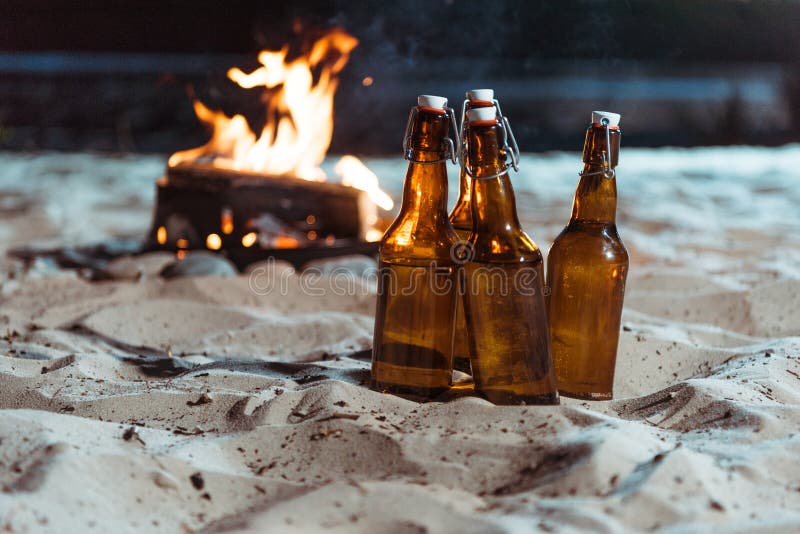 Butelki piwna pozycja na piaskowatej plaży z ogniskiem fotografia stock