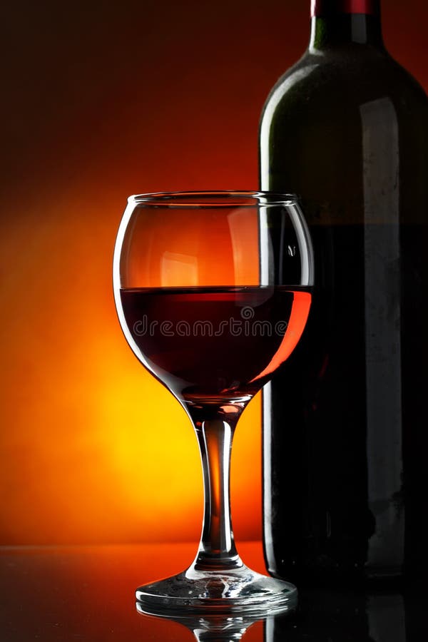 Glass and bottle of red wine over dark red background. Glass and bottle of red wine over dark red background