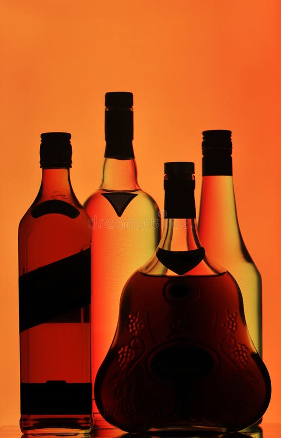 Silhouetted bottles of whiskey, cognac and vodka isolated on dim orange background. Silhouetted bottles of whiskey, cognac and vodka isolated on dim orange background