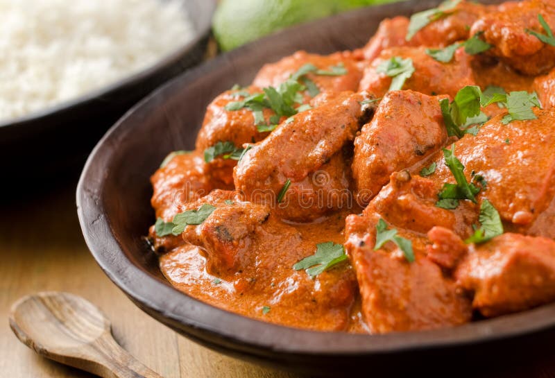 A bowl of creamy butter chicken curry with basmati rice and lime.