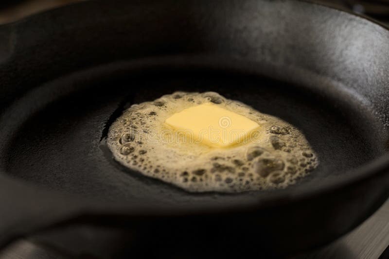 A Butter Pat Melting on a Black Cast Iron Frying Pan. Stock Image