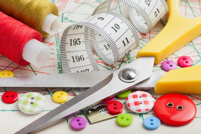 Sewing items: buttons, colorful fabrics, scissors, measuring tape, spools of thread on sewing pattern. Sewing items: buttons, colorful fabrics, scissors, measuring tape, spools of thread on sewing pattern