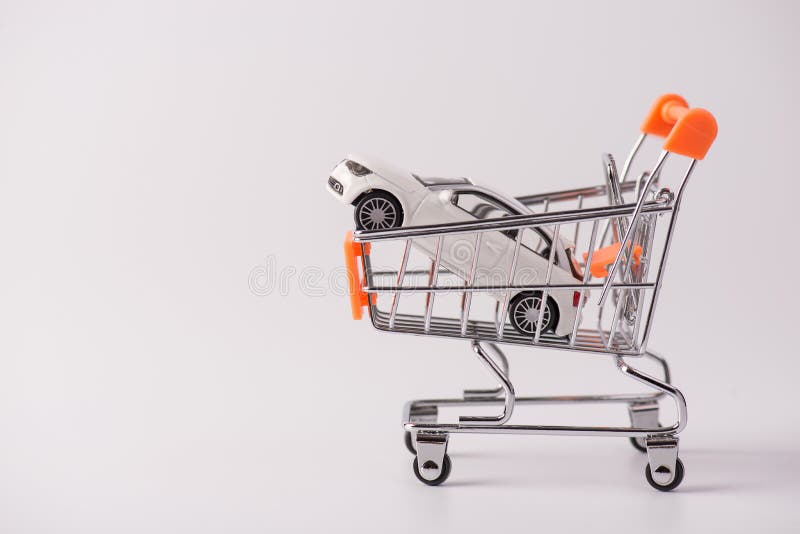 Buy new white car parking tax industry concept. Side profile close up photo of small mini toy car lying in shopping cart isolated over grey background with empty blank space.