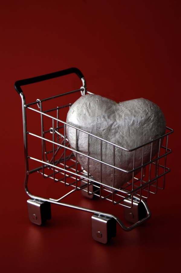 A large silver heart in a shopping cart against a deep red background. Could represent a love of shopping or trying to buy love. A large silver heart in a shopping cart against a deep red background. Could represent a love of shopping or trying to buy love.