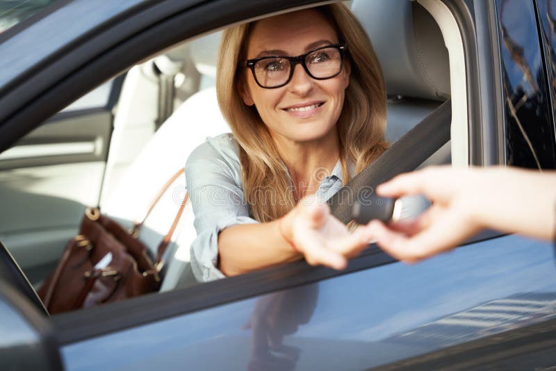 Buying a new car. Male hand giving a car keys to happy beautiful business woman sitting behind steering wheel