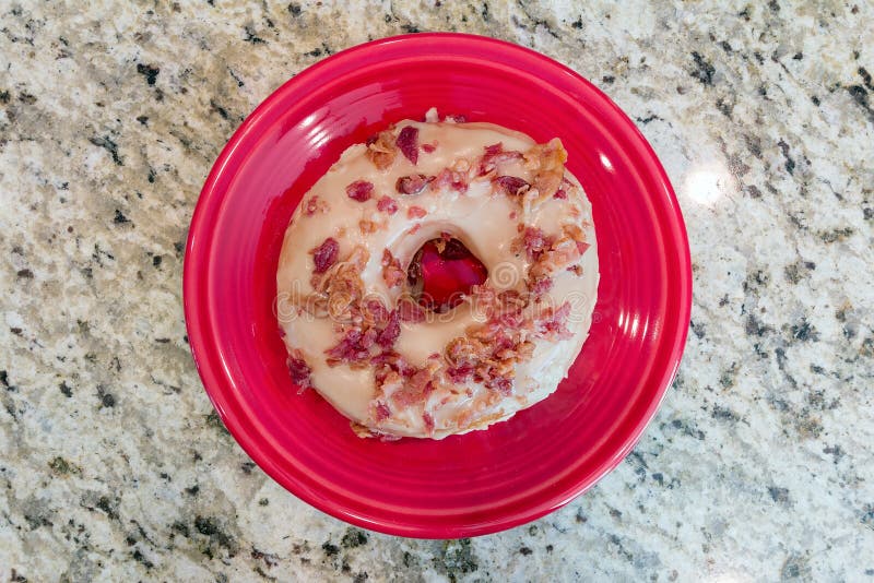 Bacon and Maple Donut on Red dessert plate with granite countertop background closeup macro. Bacon and Maple Donut on Red dessert plate with granite countertop background closeup macro