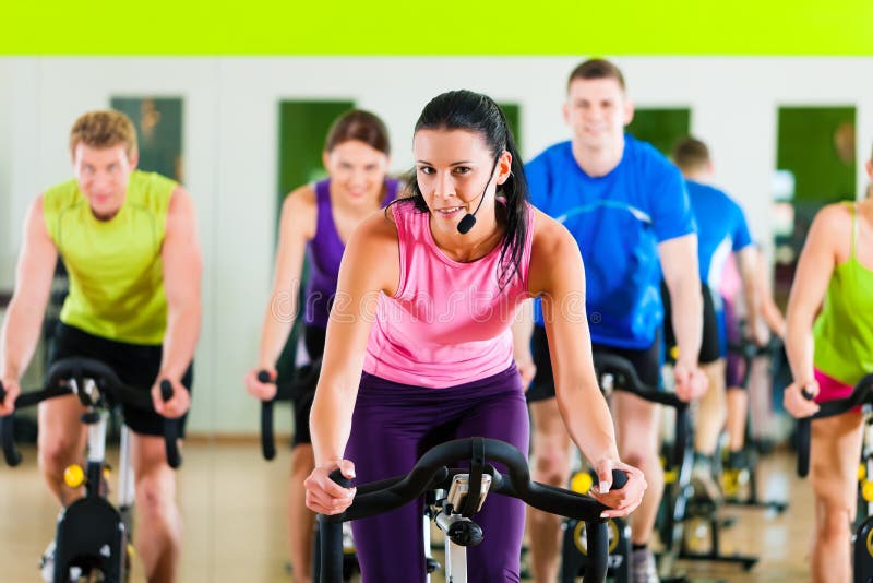 Group of five people - men and women - spinning in gym or fitness club exercising their legs doing cardio training; the trainer is in front. Group of five people - men and women - spinning in gym or fitness club exercising their legs doing cardio training; the trainer is in front