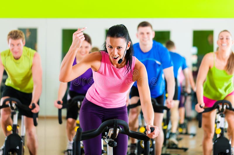 Group of five people - men and women - spinning in gym or fitness club exercising their legs doing cardio training; the trainer is in front. Group of five people - men and women - spinning in gym or fitness club exercising their legs doing cardio training; the trainer is in front