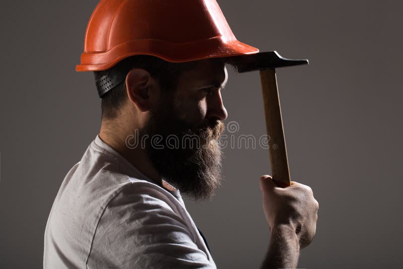 Byggmästare i hjälmen, hammare, faktotum, byggmästare i hardhat Skäggig manarbetare med skägget, byggnadshjälm, hård hatt arkivfoto Byggmästare i hjälmen, hammare, faktotum, byggmästare i hardhat Skäggig manarbetare med skägget, byggnadshjälm, hård hatt arkivfoto
