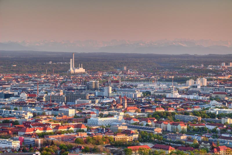 Aerial view of modern European city outskirts in evening light with industrial, commercial and residential buildings, power plant with chimneys and Bavarian Alps in background, Munchen Bayern Germany. Aerial view of modern European city outskirts in evening light with industrial, commercial and residential buildings, power plant with chimneys and Bavarian Alps in background, Munchen Bayern Germany