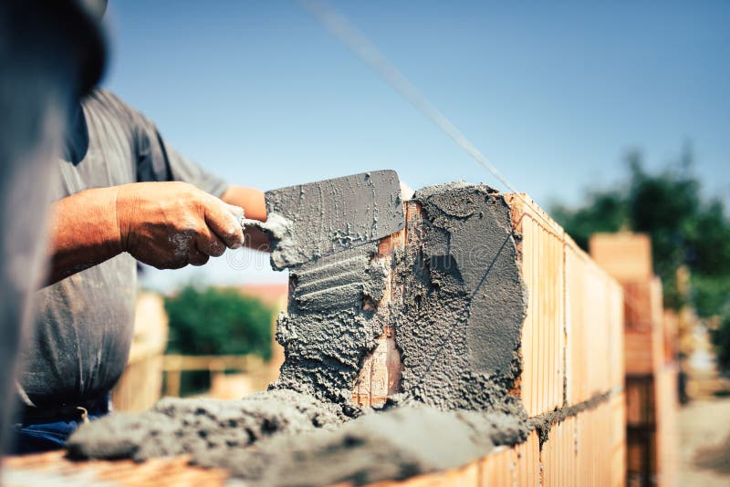 Byggnadsarbetare som installerar tegelstenmurverket på den yttre väggen med murslevspackeln
