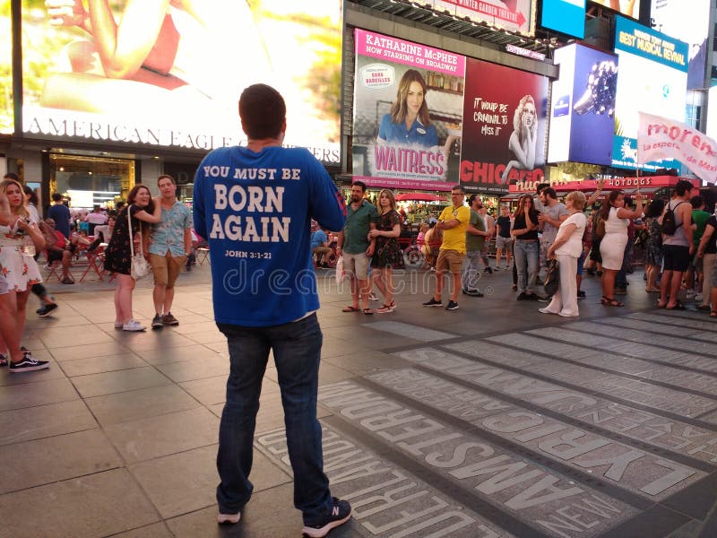 Bystanders listen to a man preaching in Times Square. On the back of the preacher`s shirt, a quote from John - `You Must Be Born Again`. This photo was taken in New York City on July 2nd 2018. Bystanders listen to a man preaching in Times Square. On the back of the preacher`s shirt, a quote from John - `You Must Be Born Again`. This photo was taken in New York City on July 2nd 2018.