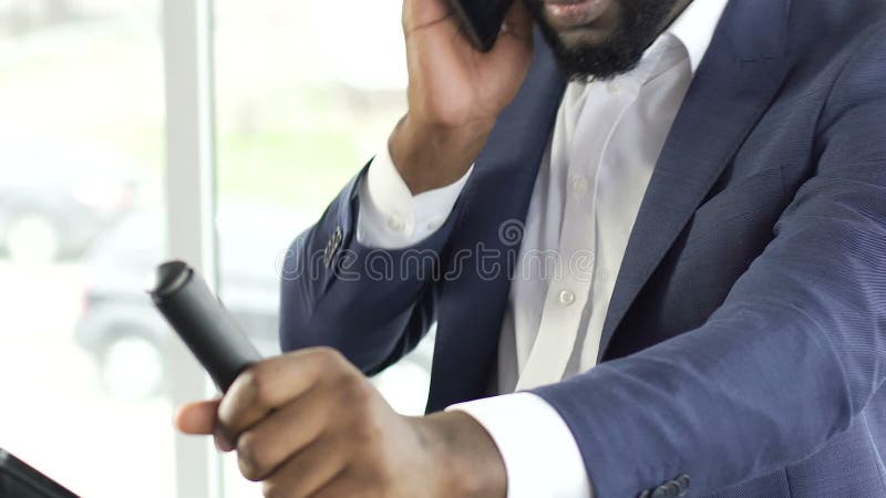 Bärande affärsdräkt för svart man som övar på den stationära cykeln som talar på telefonen